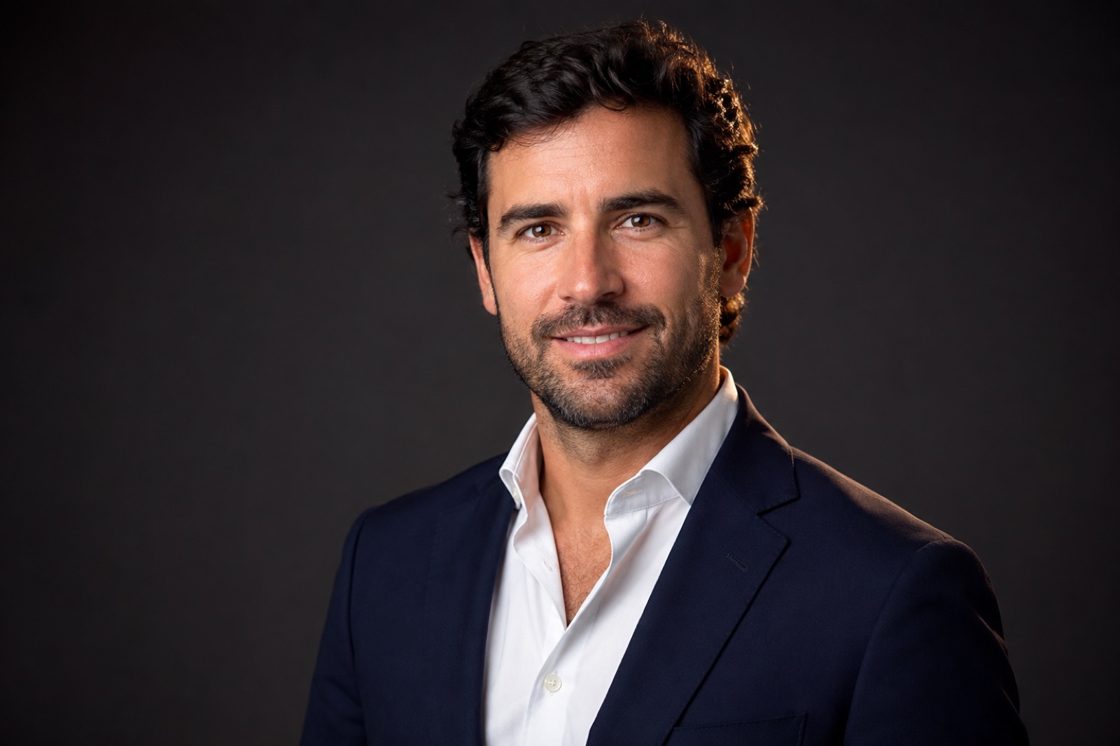 Retrato corporativo de un hombre con traje azul marino sobre fondo gris