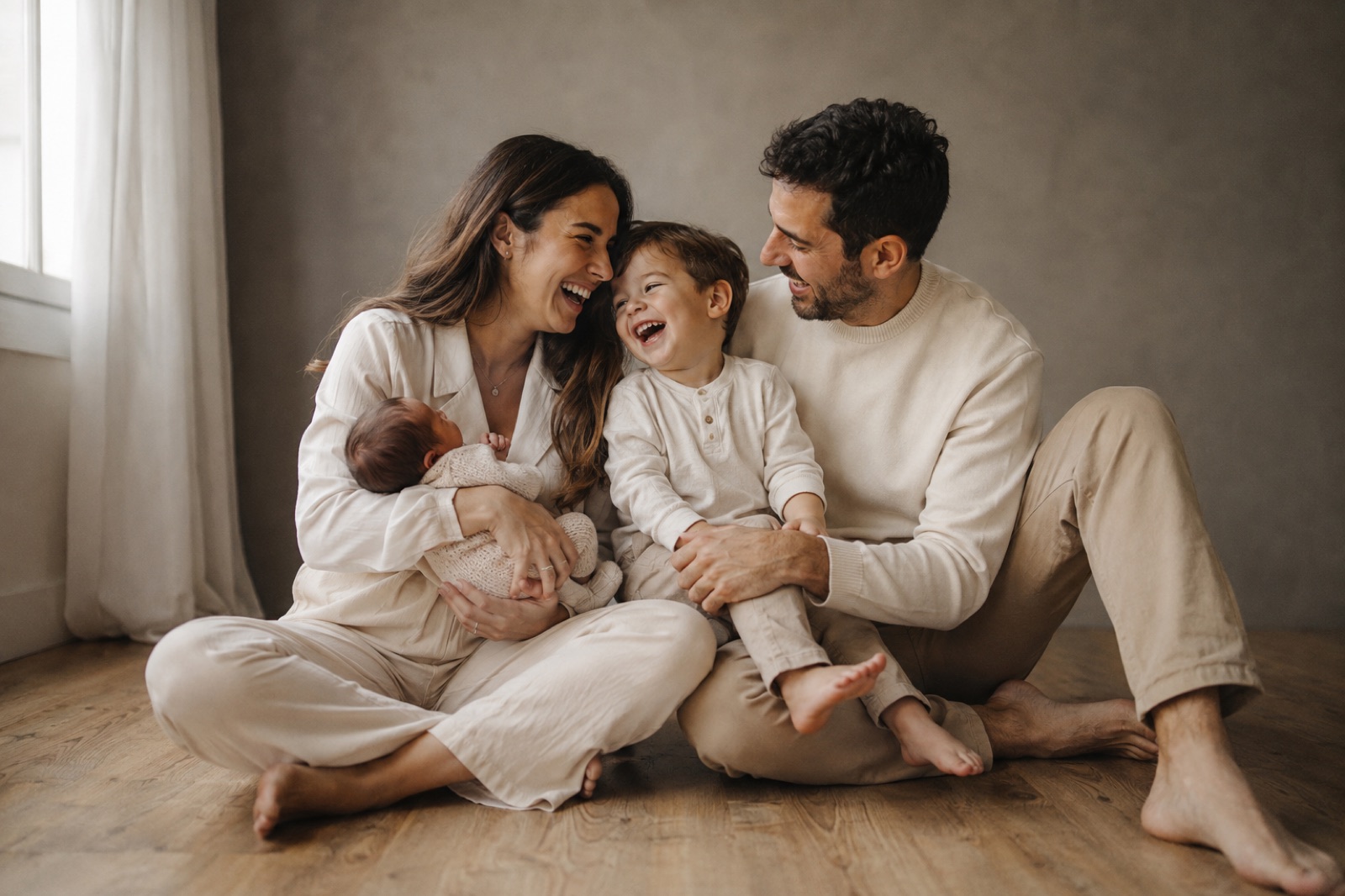Familia joven con bebé riendo sobre fondo gris cálido en el estudio